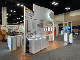 RENTAL: 10 x 20 Island Design with Curved Double-Sided Gravitee Wall Structure, L-Shaped Kiosk Product Display, (4) RE-1594 White Laminated Workstation Counters with Recessed LED/RGB Lighting, RE-1572 L-Shaped Backlit Reception Counter with White Laminate